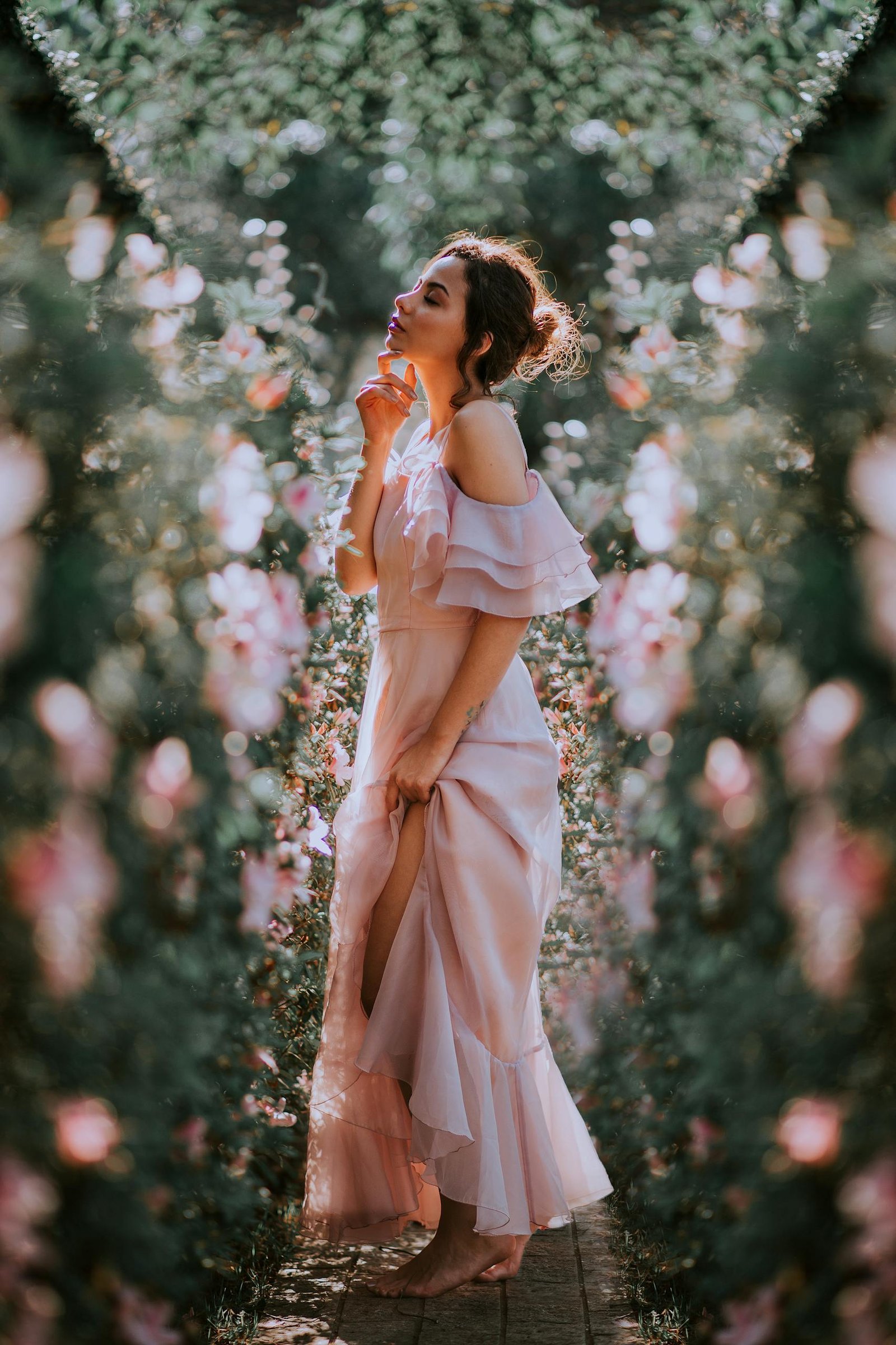 A woman in a pink dress posing thoughtfully in a lush floral garden.