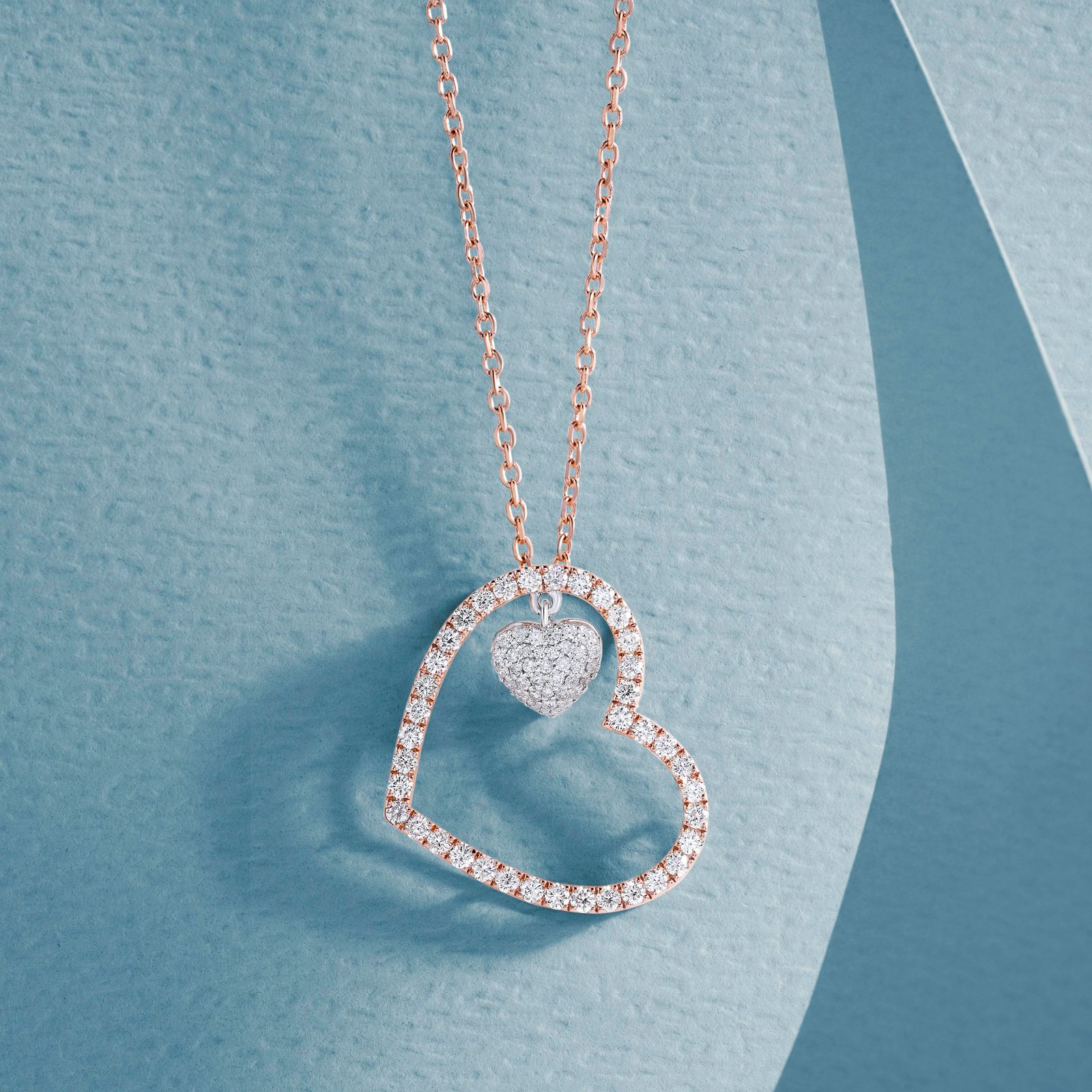Close-up of a luxurious heart-shaped diamond pendant on a gold chain against a textured blue backdrop.