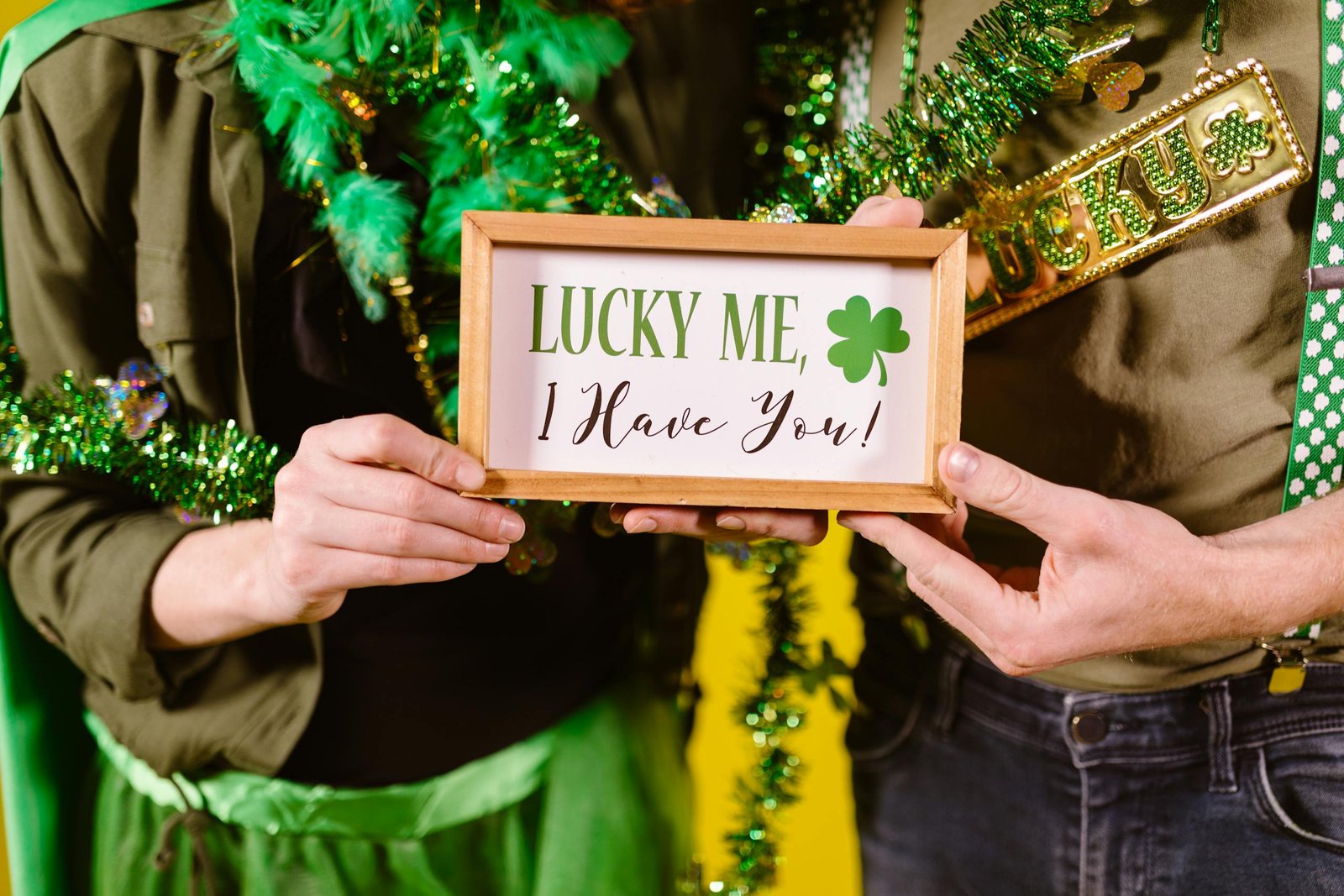 Two people holding a festive St. Patrick's Day sign with decorations.